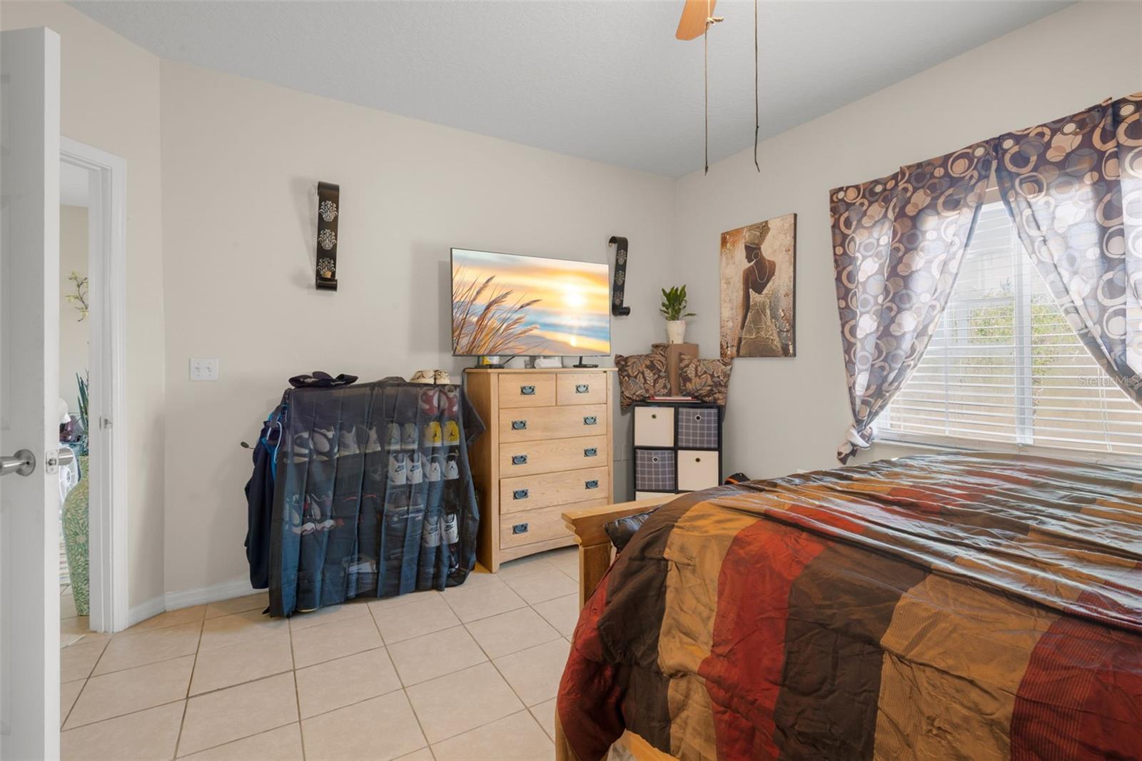 Light-filled primary bedroom featuring ceramic tile flooring and a generous layout that accommodates full-size furnishings with ease. A large window provides natural light, while the neutral color palette offers flexibility for any décor style. The suite includes direct access to the en suite bath and walk-in closet, enhancing privacy and everyday convenience within the split-bedroom floor plan.