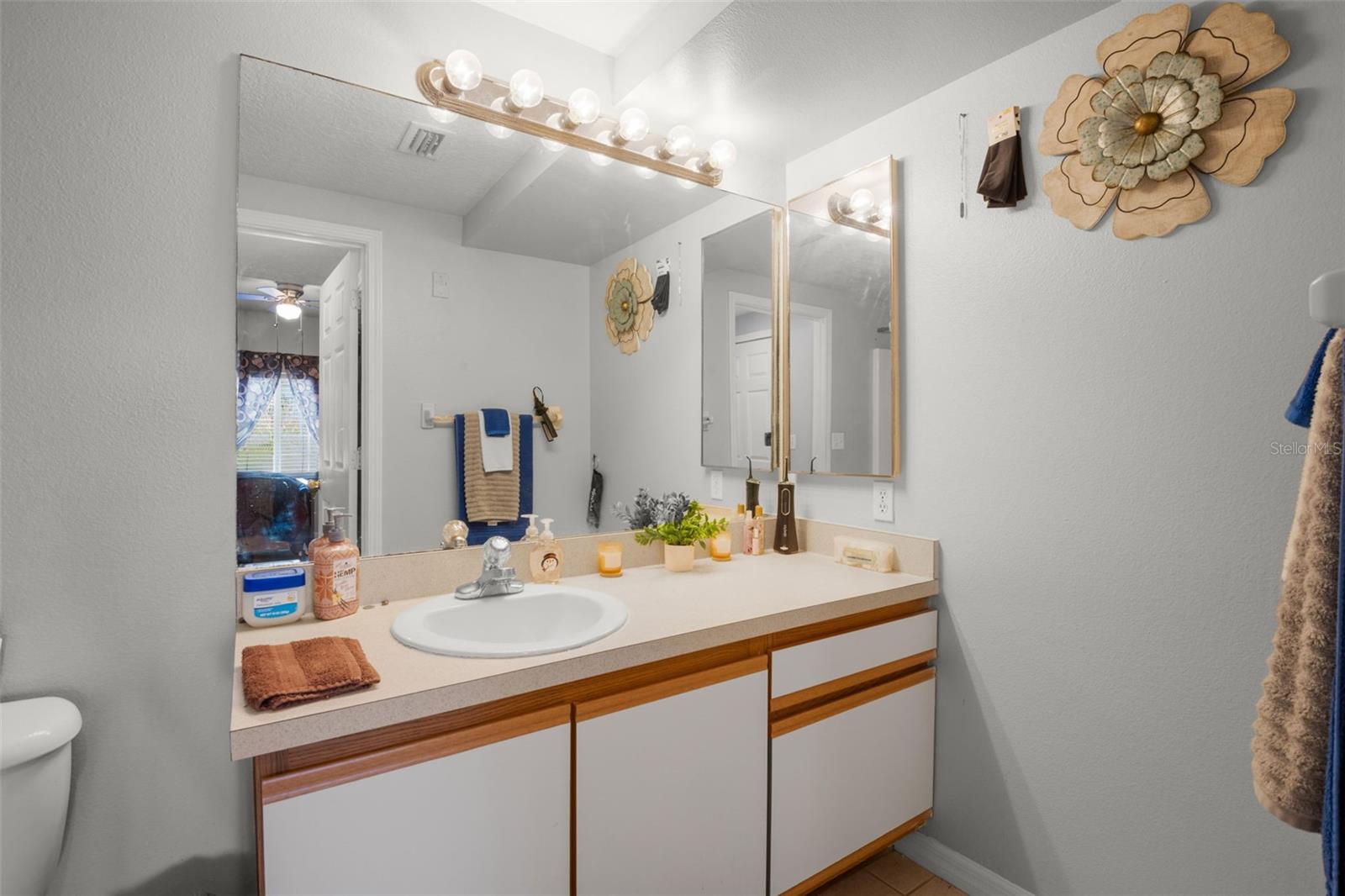 Primary ensuite bath featuring an extended vanity with ample counter space, large wall-to-wall mirror, and overhead lighting. Neutral cabinetry and finishes create a bright, functional space with convenient storage below.