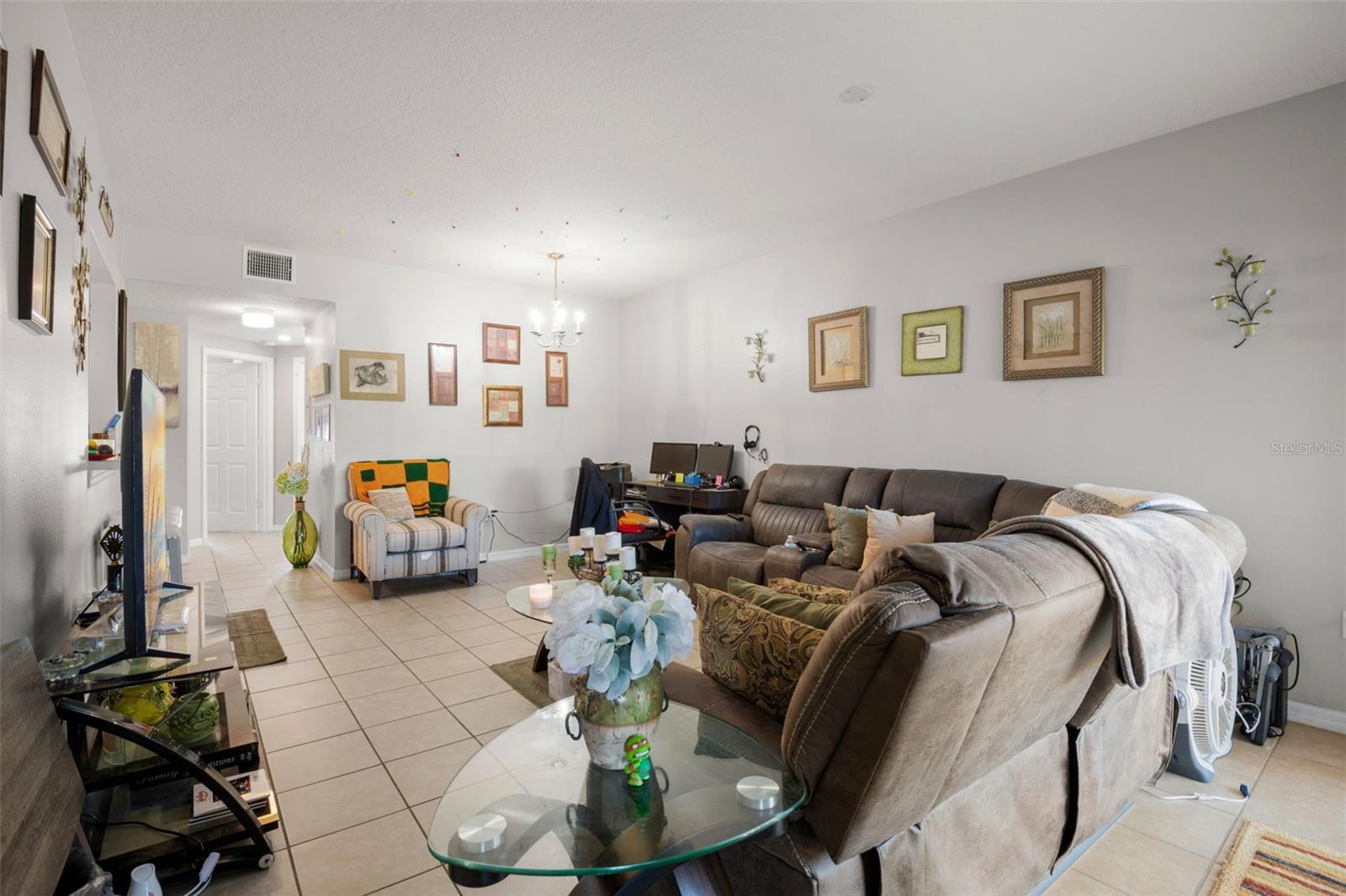 Expansive open living and dining layout featuring continuous ceramic tile flooring and a light, neutral color palette. The elongated design provides flexibility for multiple seating arrangements