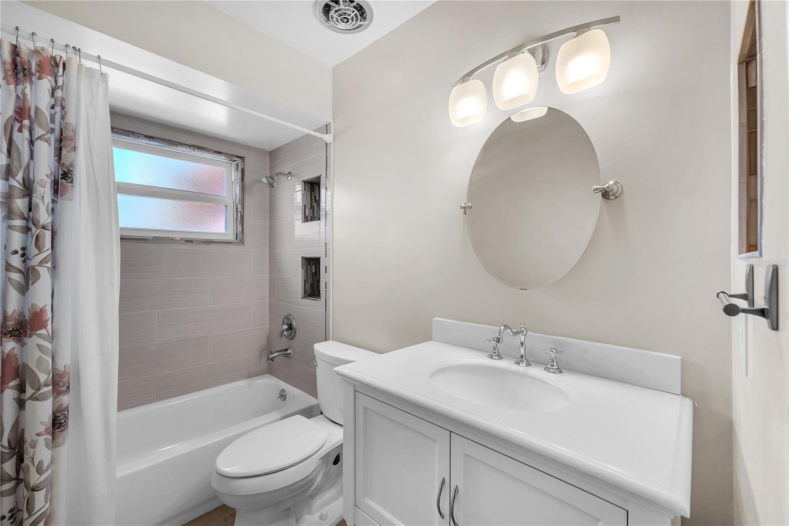 The guest bathroom is beautifully updated with a tub/shower combination, custom cabinetry with a Corian countertop, a frameless adjustable mirror, and convenient built-in storage niches.