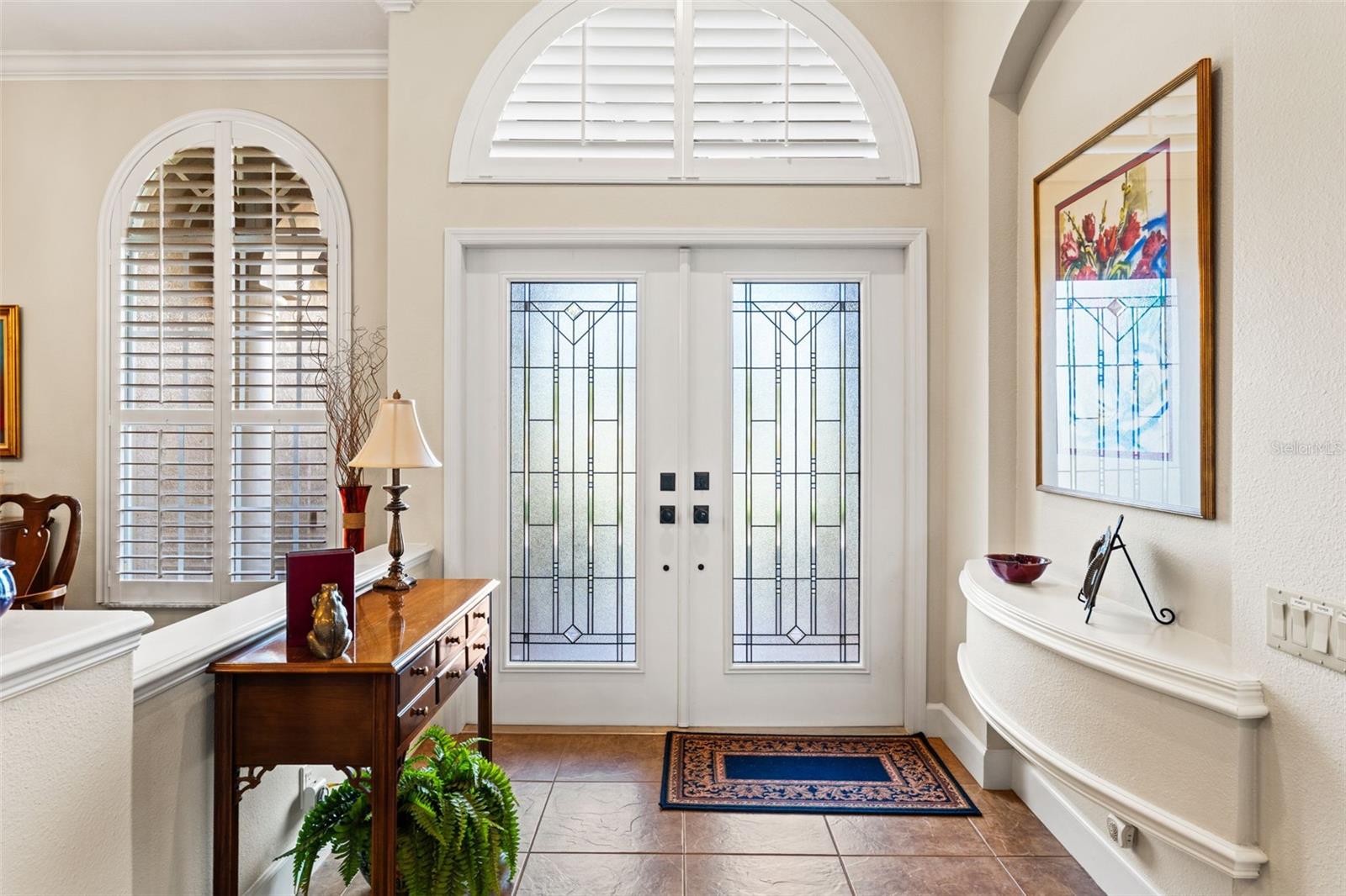 A bright and welcoming foyer features double glass entry doors, arched transom windows, and elegant architectural detailing that sets the tone upon arrival.