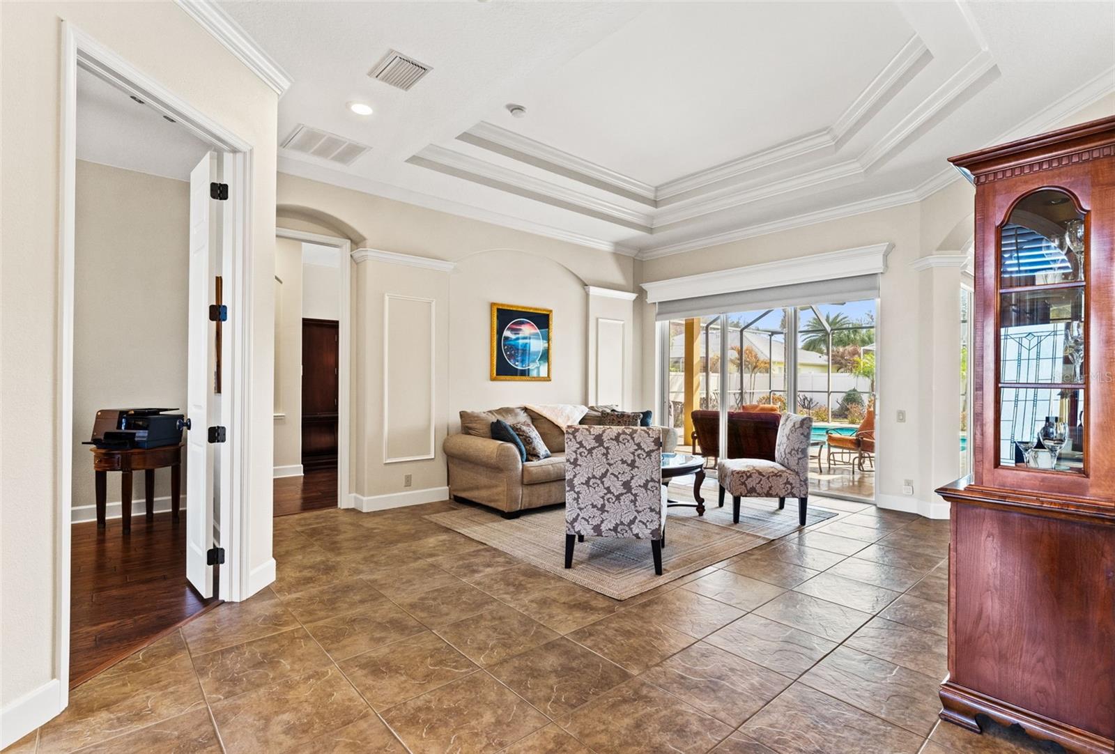 This inviting living space features tray ceilings, crown molding, and large sliding glass doors that fill the room with natural light and offer seamless access to the outdoor living area.