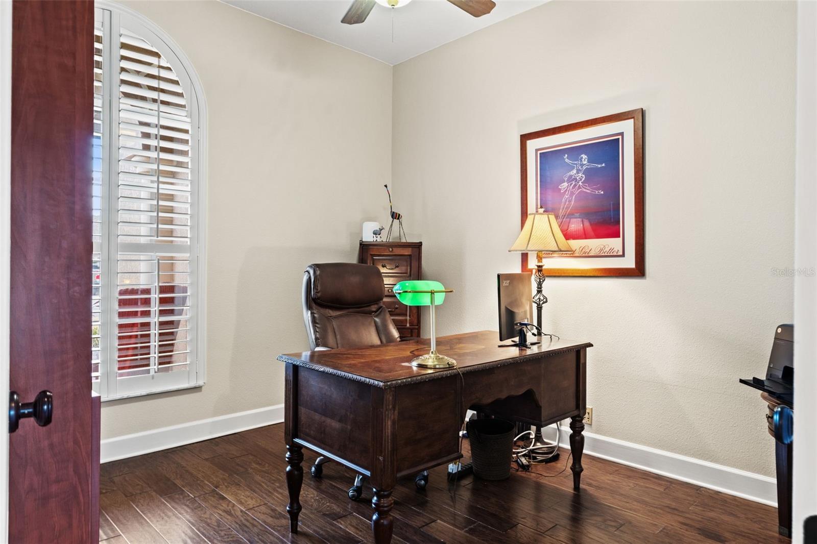 A dedicated office with rich wood flooring and plantation shutters provides a comfortable and functional space for remote work or study.