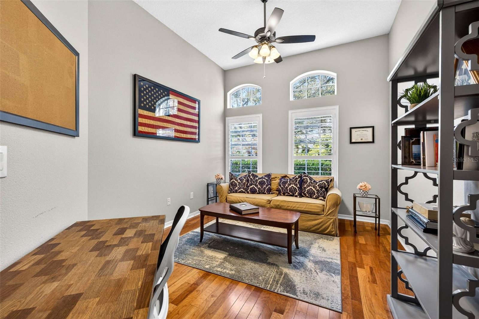 Office with ceiling fan, plantation shutters and hardwood flooring.