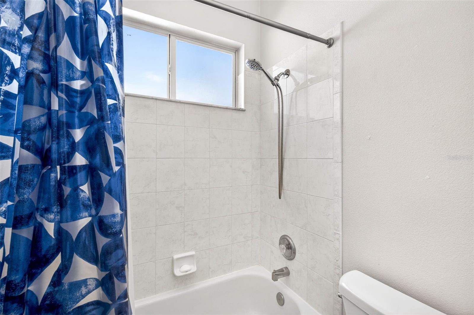 Secondary bathroom with handheld showerhead and window providing natural lighting