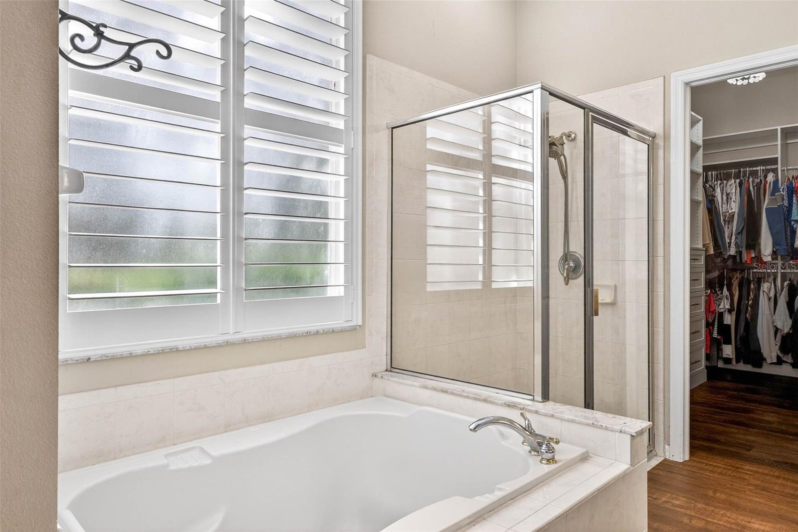 Garden tub situated under grand window with plantation shutters.