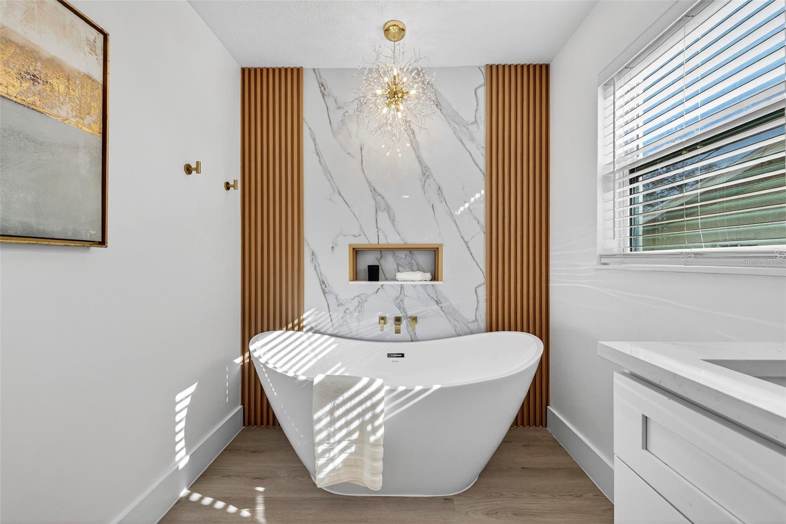 Deep FREESTANDING SOAKING TUB surrounded by elegant custom tile and a stunning chandelier.