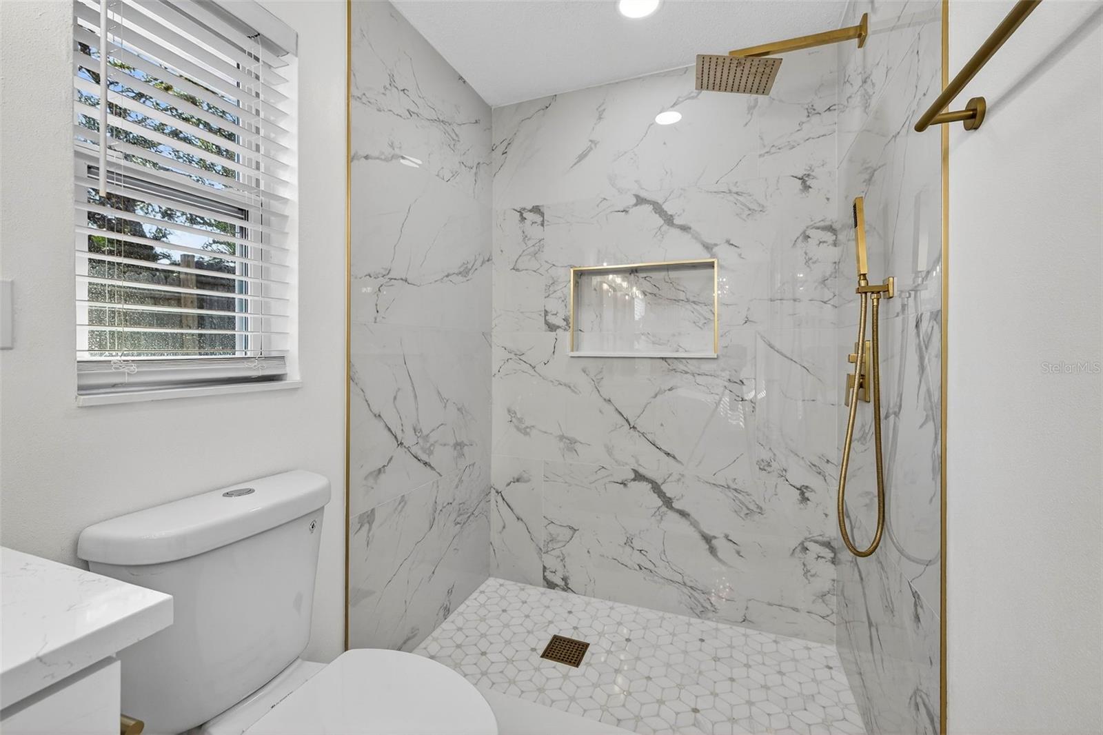 Spa-inspired primary bathroom with separate tub and custom-tiled shower with gold fixtures on the other side.