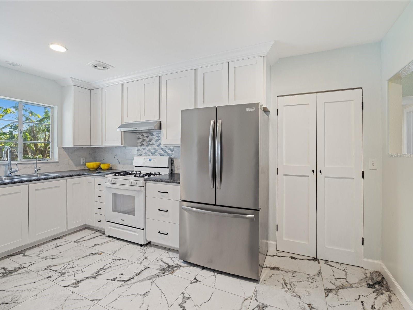 Kitchen with real wood cabinets, custom pantry, gas stove and hood vent, stylish tiled backsplash, stainless refrigerator, touchless faucet and water filtration system.