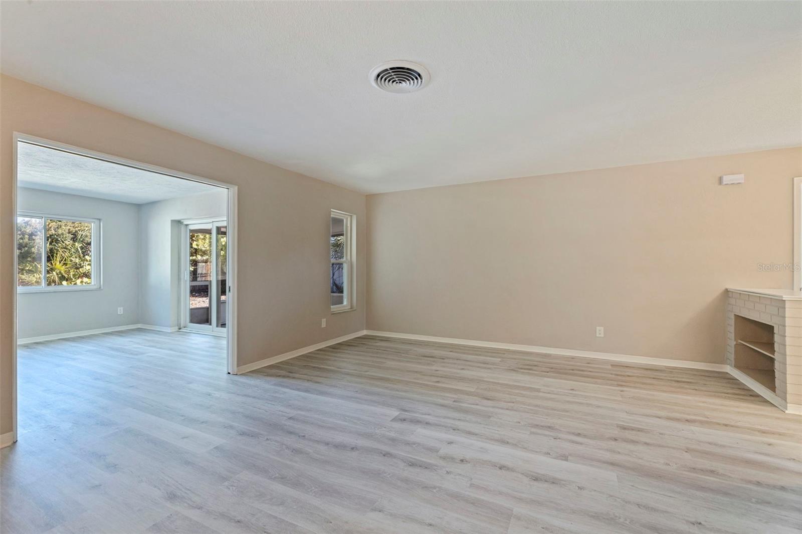 Spacious living room featuring updated vinyl plank flooring and neutral finishes, with flexible layout options for seating and entertainment. Double pocket doors provide a wide opening into the adjacent Florida room, allowing for seamless flow or the option to create a more private retreat. The Florida room is filled with natural light from surrounding windows and offers direct access to the screened porch, extending the living space for year-round enjoyment.