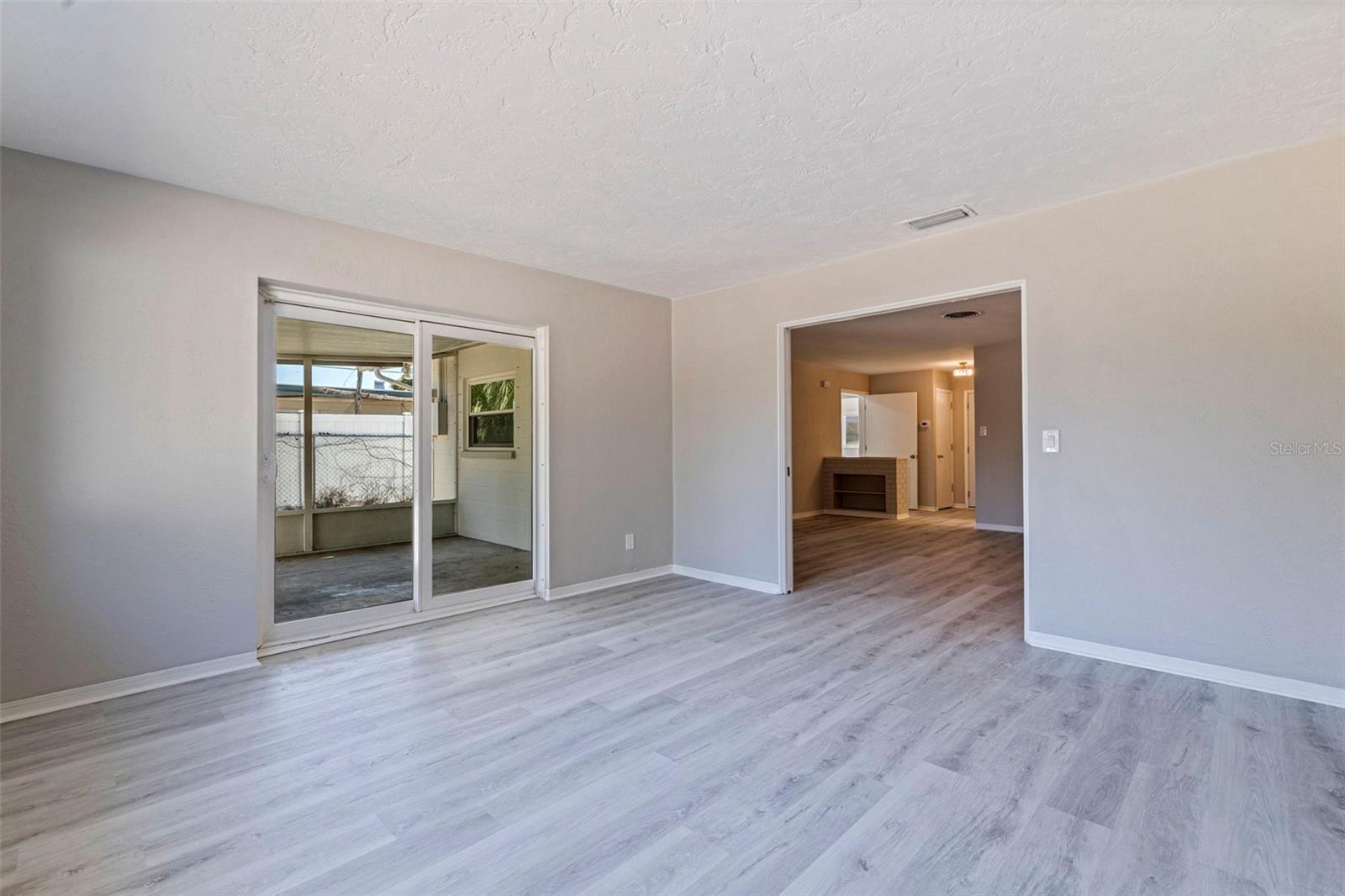 Spacious Florida room with updated vinyl plank flooring and neutral finishes, offering flexible use as a second living area, home office, or media space. Sliding glass doors provide direct access to the screened porch, creating an easy indoor-outdoor connection. Wide opening to the main living area allows for an open feel while maintaining the option for separation.