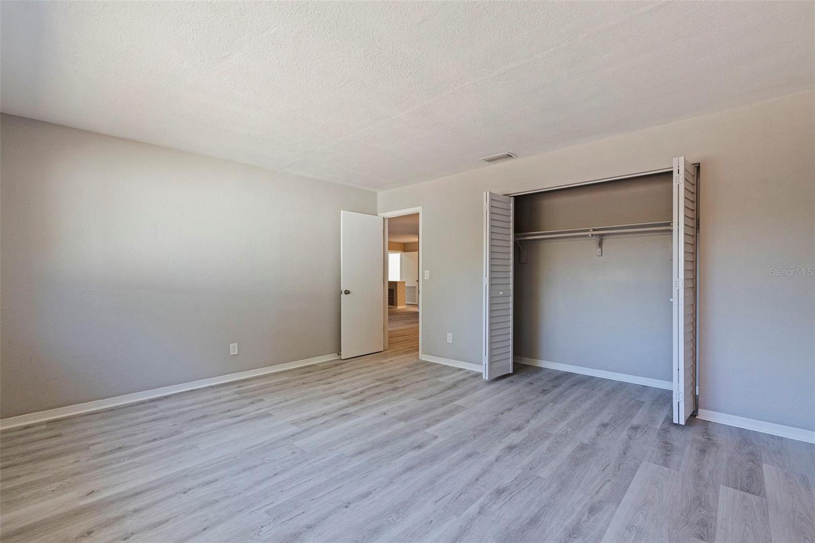 Generously sized primary bedroom with updated vinyl plank flooring and neutral finishes throughout. The open layout offers flexibility for a full bedroom suite, while the wide closet with bifold doors provides ample hanging and storage space.