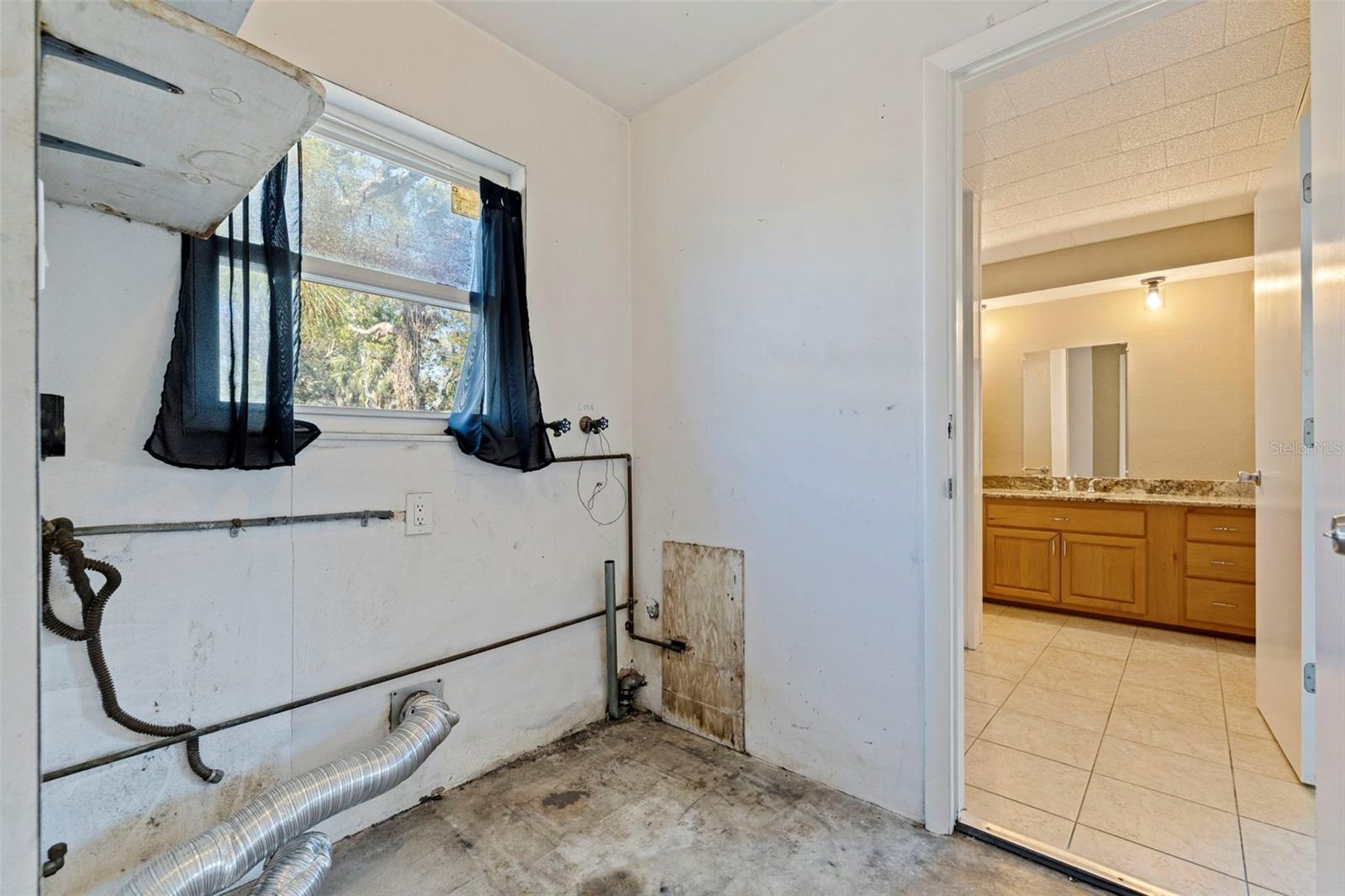 Laundry room off the garage with washer and dryer hookups and dedicated utility connections in place. A window provides natural light and ventilation, while direct access to the primary bath adds functional convenience. Practical layout offers space for full-size appliances and additional storage or shelving.