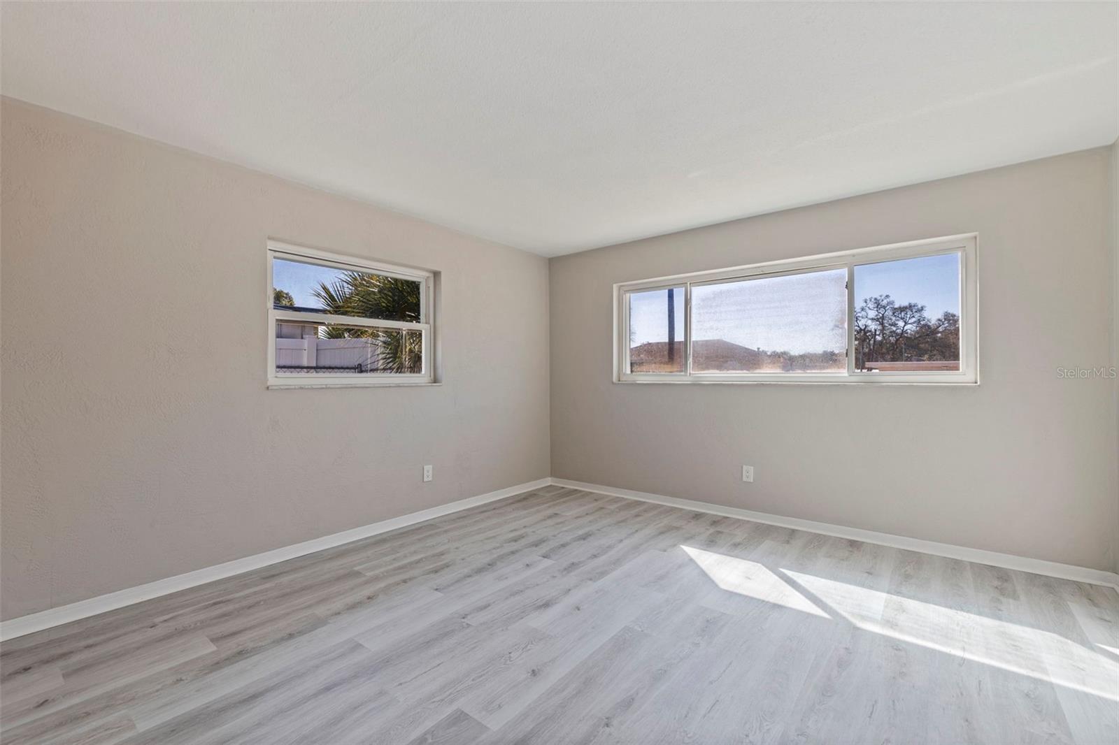 Bedroom 2 featuring updated vinyl plank flooring and a bright, open layout. Dual windows provide natural light, creating an inviting space ideal for guests, family, or a home office. Neutral finishes offer a clean backdrop ready for personalization.