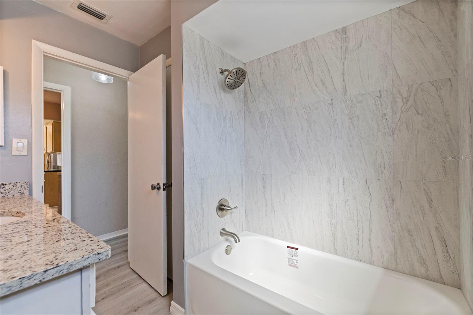 Second bathroom with a tub and shower combination featuring a marble-style tile surround and updated brushed-nickel fixtures. The clean lines and neutral palette create a bright, modern feel, complemented by the adjacent granite vanity for a cohesive, updated look.