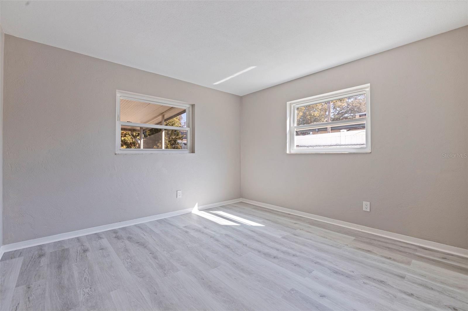 Bedroom 3 featuring updated vinyl plank flooring and a bright, neutral interior. Dual windows provide natural light and backyard views, creating a comfortable space ideal for a guest room, nursery, or home office. Clean lines and a versatile layout offer flexibility for a variety of needs.