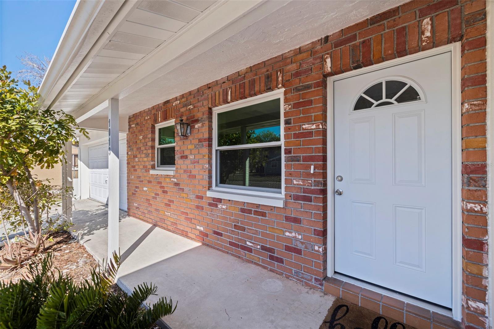 Covered front entrance with brick accent wall and sheltered concrete porch. Updated front door with semi-circle window detail provides natural light while maintaining privacy. Dual front-facing windows enhance the entry façade, and the protected alcove design offers convenient, weather-shielded access directly from the driveway and garage.