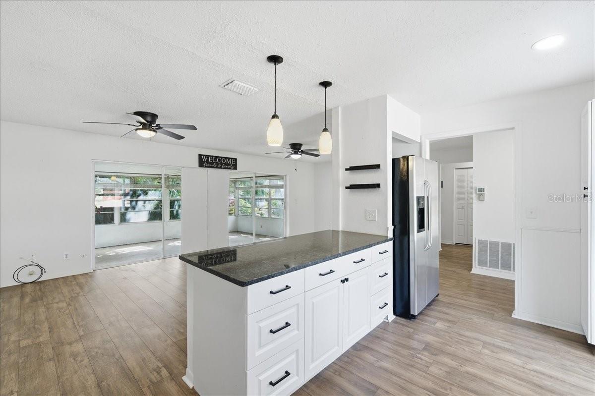 The updated kitchen is bright and welcoming, featuring white cabinetry, two windows, a dinette area, and a prep counter with pendant lighting that opens to the dining area. Black accents and stainless-steel appliances create a crisp, modern look. Ample cabinetry, generous counter space, and direct garage entry combine to create a kitchen designed for both daily living and easy entertaining.