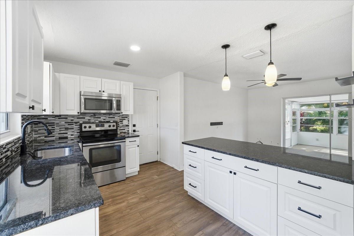The updated kitchen is bright and welcoming, featuring white cabinetry, two windows, a dinette area, and a prep counter with pendant lighting that opens to the dining area. Black accents and stainless-steel appliances create a crisp, modern look. Ample cabinetry, generous counter space, and direct garage entry combine to create a kitchen designed for both daily living and easy entertaining.