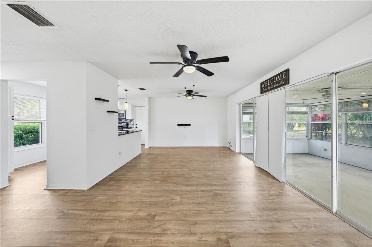 The open living room and dining room combination features a wall of glass sliders that flood the space with natural light and showcase peaceful views of the enclosed lanai and backyard. New laminate flooring extends throughout the main living areas and into the kitchen.