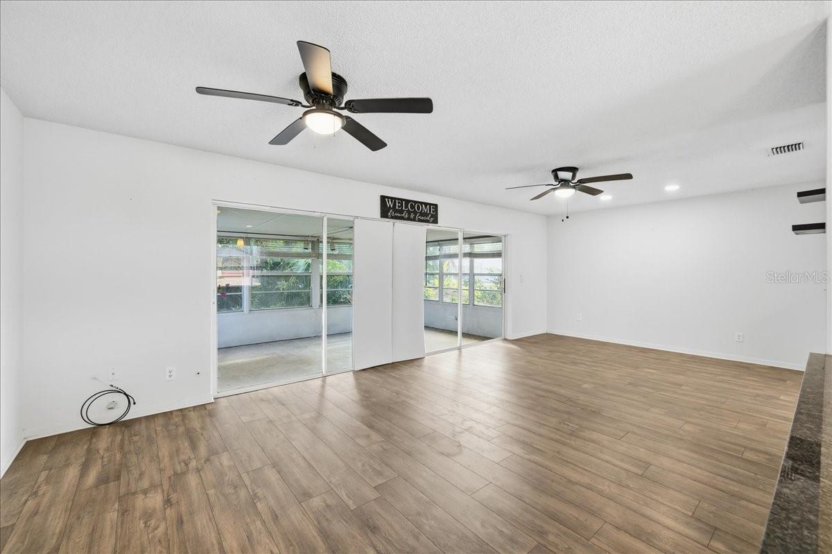 The open living room and dining room combination features a wall of glass sliders that flood the space with natural light and showcase peaceful views of the enclosed lanai and backyard. New laminate flooring extends throughout the main living areas and into the kitchen.