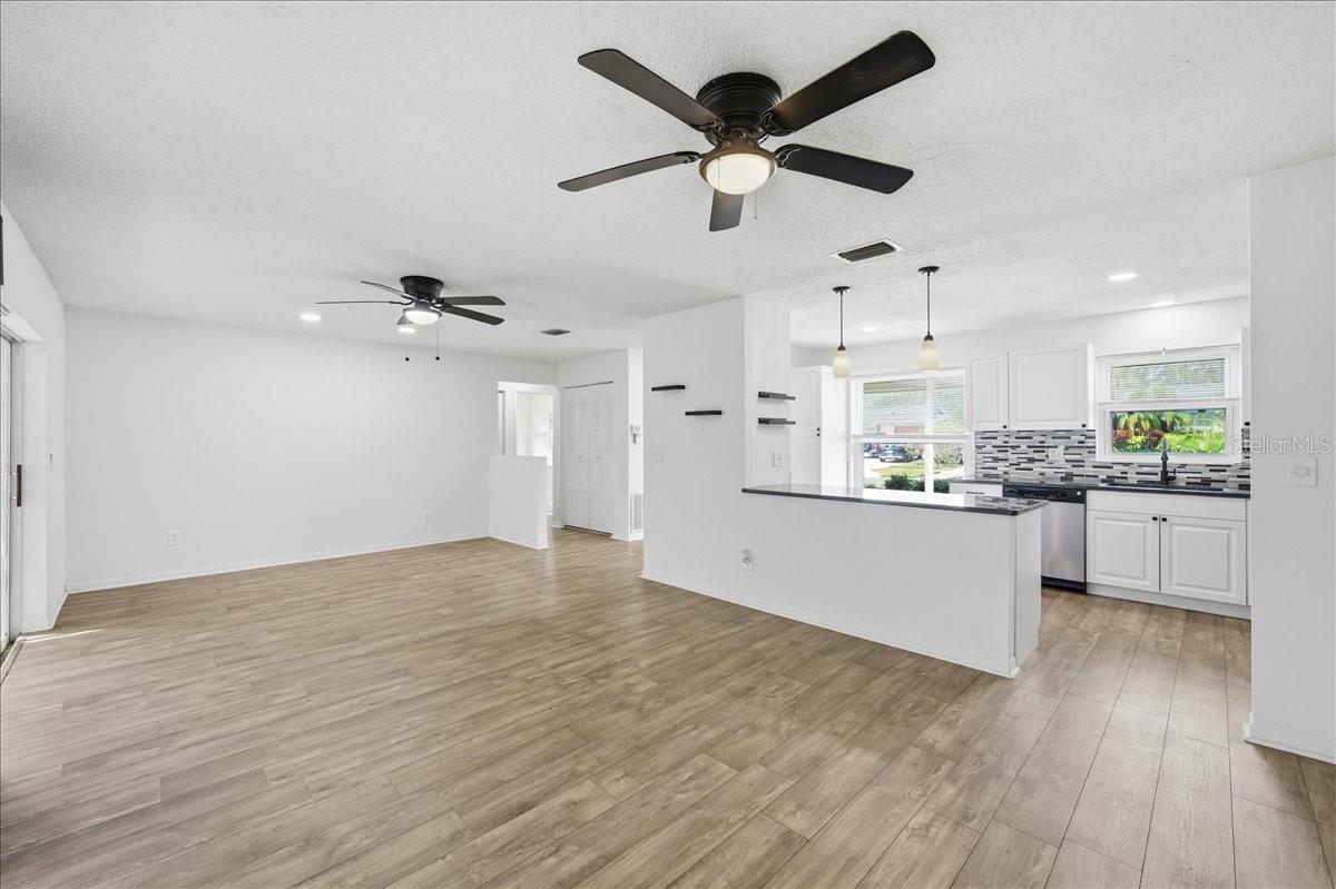 The open living room and dining room combination features a wall of glass sliders that flood the space with natural light and showcase peaceful views of the enclosed lanai and backyard. New laminate flooring extends throughout the main living areas and into the kitchen.