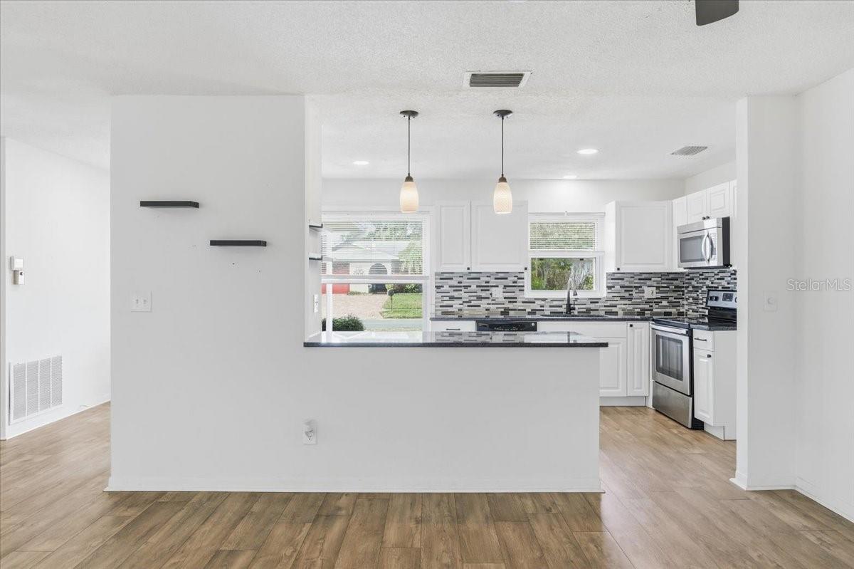 The open living room and dining room combination features a wall of glass sliders that flood the space with natural light and showcase peaceful views of the enclosed lanai and backyard. New laminate flooring extends throughout the main living areas and into the kitchen.