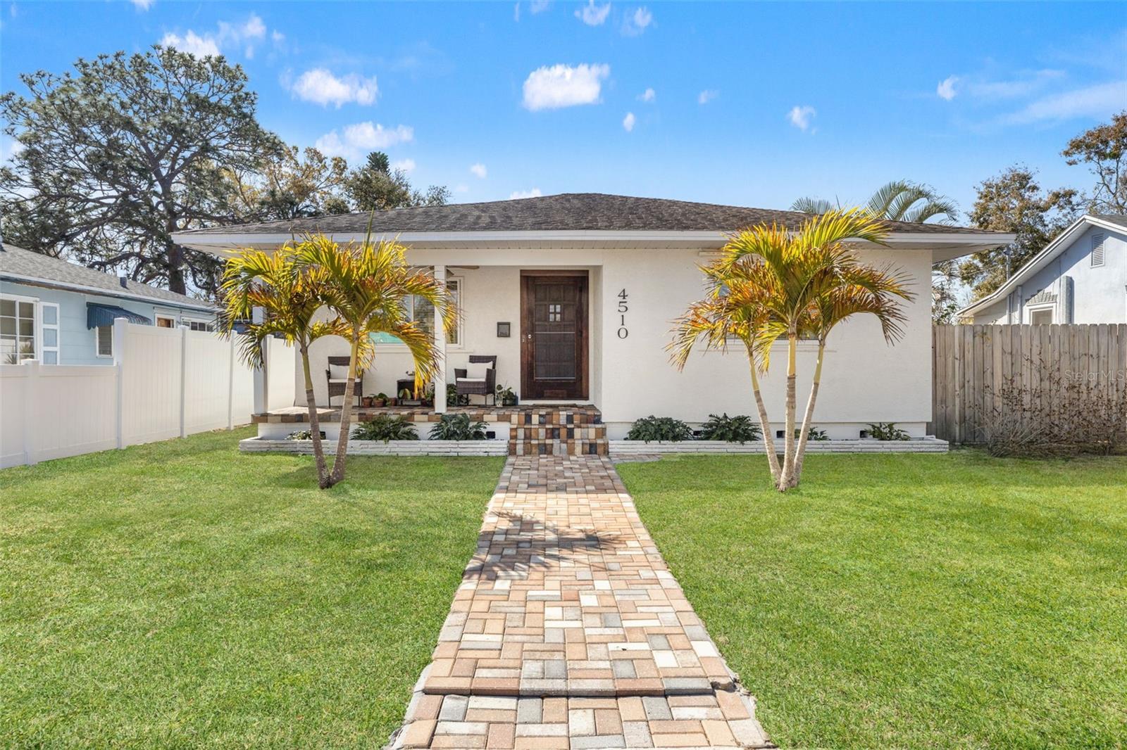 Charming single-story home with a clean stucco façade and welcoming covered front porch, framed by manicured landscaping and palm trees for added curb appeal.