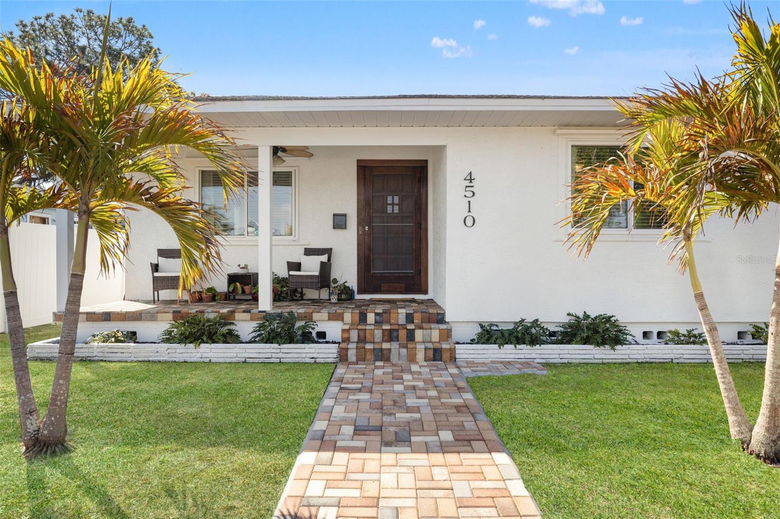 The symmetrical front design features a rich wood entry door, updated paver steps, and fresh landscaping for a well-maintained first impression.
