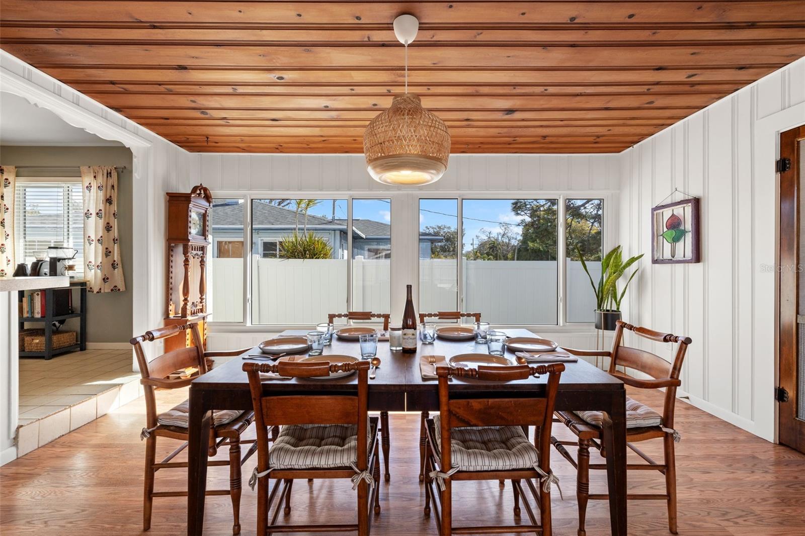 Inviting dining space highlighted by a warm wood plank ceiling, statement woven pendant light, and a full wall of windows that bring in abundant natural light. The spacious layout easily accommodates gatherings while offering peaceful views of the backyard.