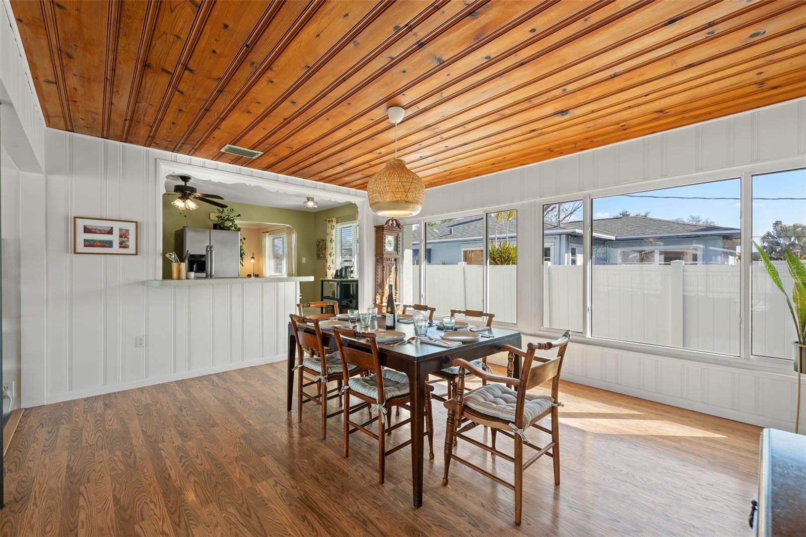 Spacious dining area with a striking wood plank ceiling, statement pendant lighting, and expansive windows that fill the room with natural light. The open layout connects seamlessly to the kitchen, creating an ideal setting for everyday meals or entertaining.