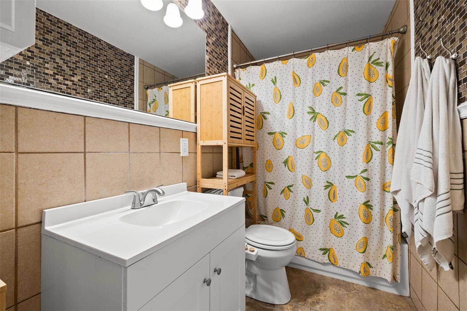 Well-appointed bathroom featuring a modern vanity with updated fixtures, tiled walls, and a full shower-tub combination. Functional layout with ample storage and clean, neutral finishes.