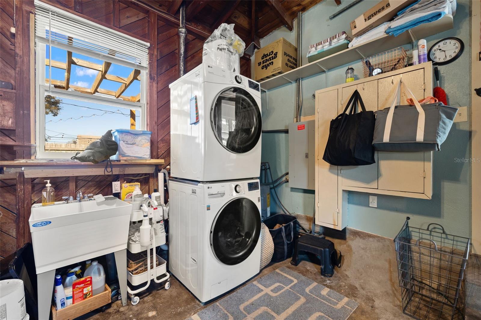 Convenient in-garage laundry area with utility sink, stacked washer and dryer, and open shelving for added storage. Practical layout designed to keep household tasks organized and efficient.