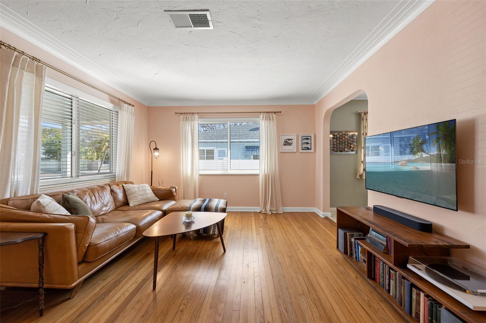 Bright and welcoming living room featuring warm hardwood floors, soft neutral tones, and abundant natural light from multiple windows.