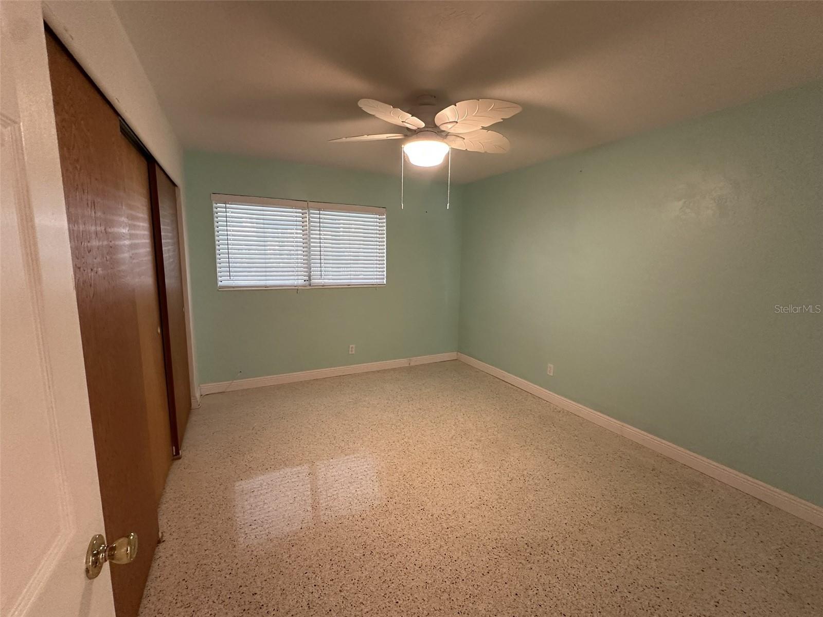 Primary Bedroom with terrazzo flooring, decorative ceiling fan, and window to FL Room providing natural light.
