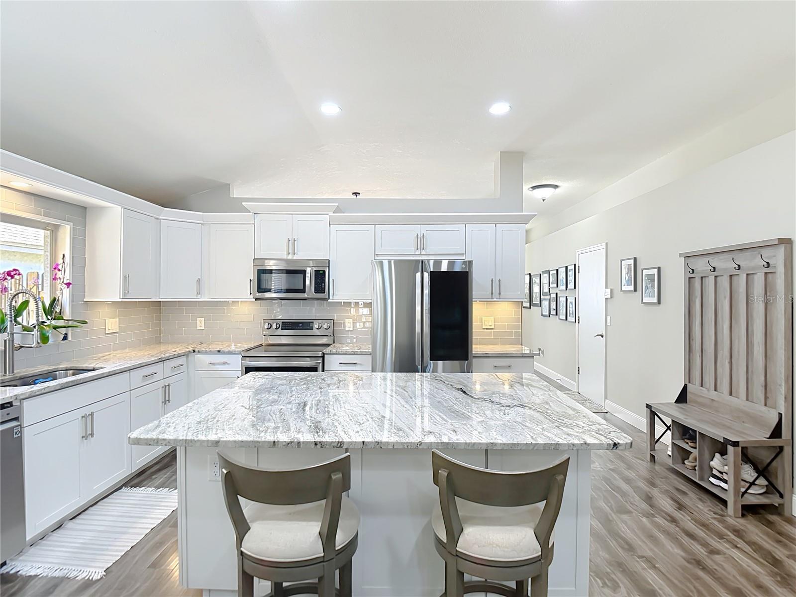 The fully remodeled kitchen (2021) is the heart of the home, featuring white cabinetry with modern hardware, granite countertops, glass subway tile backsplash, a large center island with built-in wine refrigerator, and stainless-steel LG appliances.