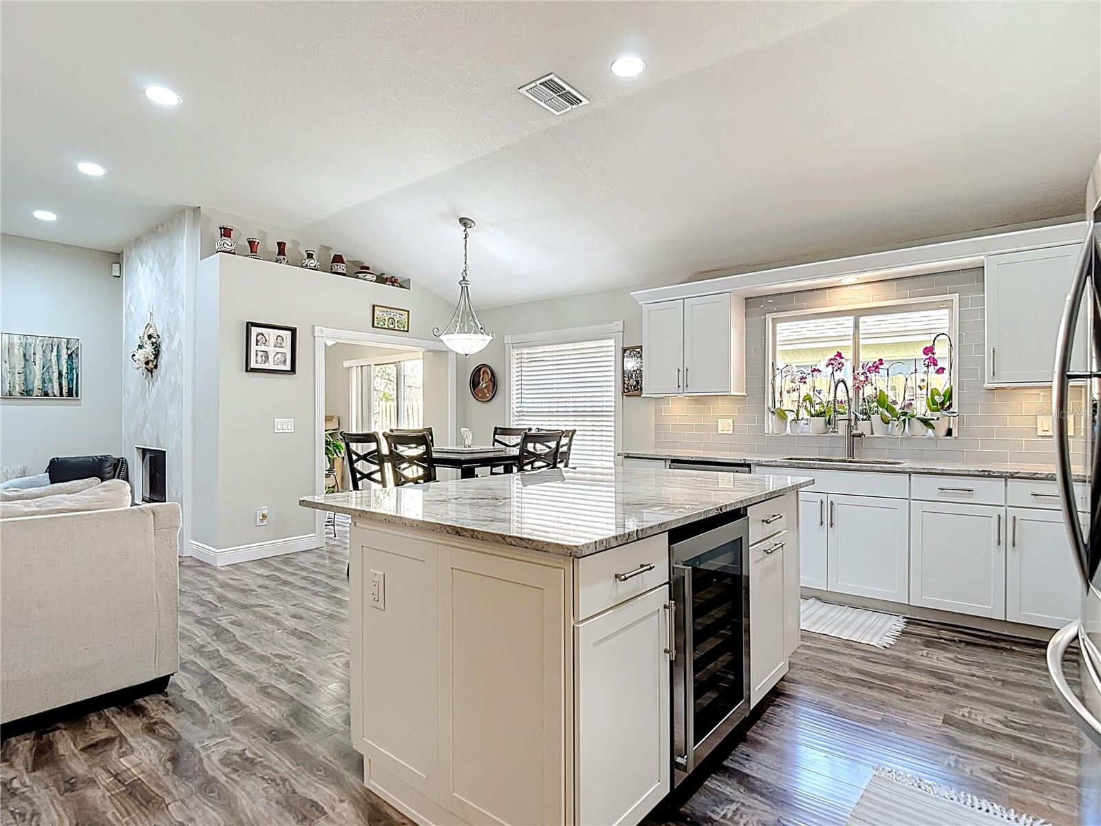 The fully remodeled kitchen (2021) is the heart of the home, featuring white cabinetry with modern hardware, granite countertops, glass subway tile backsplash, a large center island with built-in wine refrigerator, and stainless-steel LG appliances.