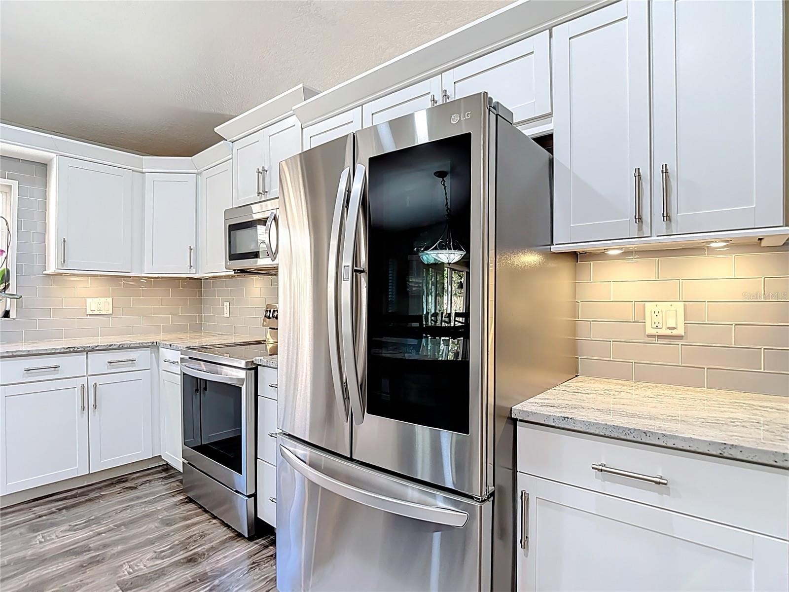 The fully remodeled kitchen (2021) is the heart of the home, featuring white cabinetry with modern hardware, granite countertops, glass subway tile backsplash, a large center island with built-in wine refrigerator, and stainless-steel LG appliances.