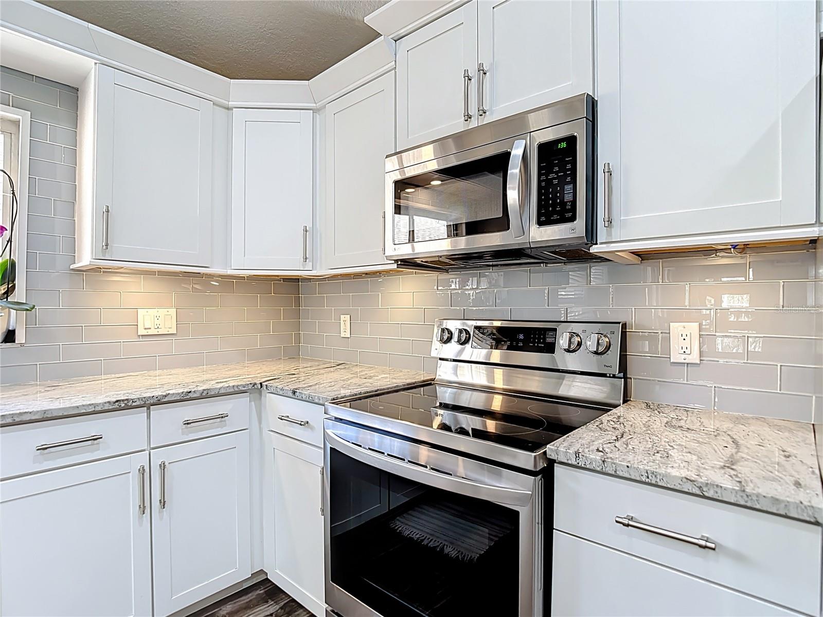 The fully remodeled kitchen (2021) is the heart of the home, featuring white cabinetry with modern hardware, granite countertops, glass subway tile backsplash, a large center island with built-in wine refrigerator, and stainless-steel LG appliances.