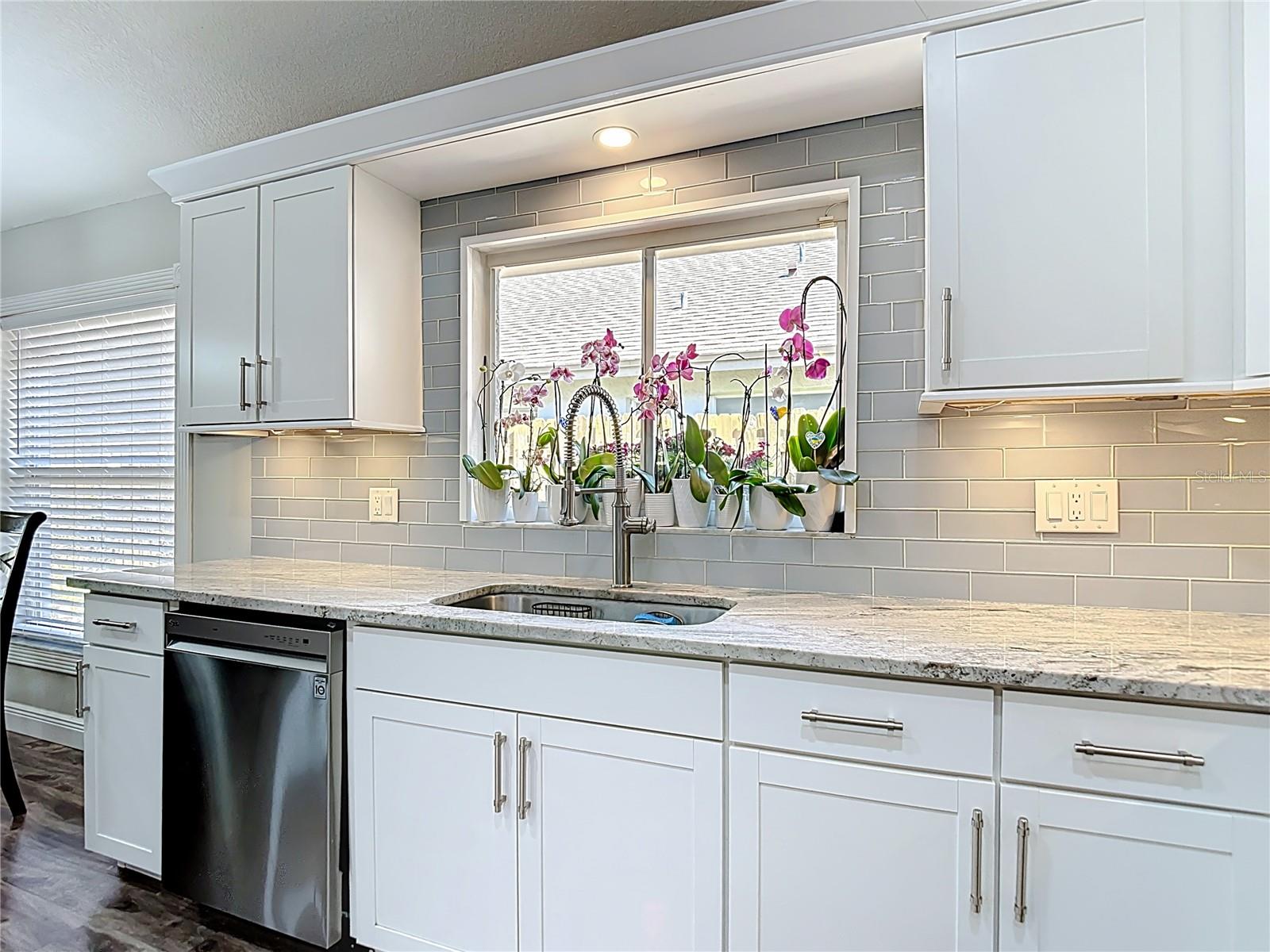 The fully remodeled kitchen (2021) is the heart of the home, featuring white cabinetry with modern hardware, granite countertops, glass subway tile backsplash, a large center island with built-in wine refrigerator, and stainless-steel LG appliances.