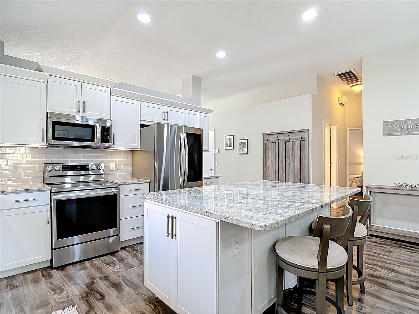 The fully remodeled kitchen (2021) is the heart of the home, featuring white cabinetry with modern hardware, granite countertops, glass subway tile backsplash, a large center island with built-in wine refrigerator, and stainless-steel LG appliances.