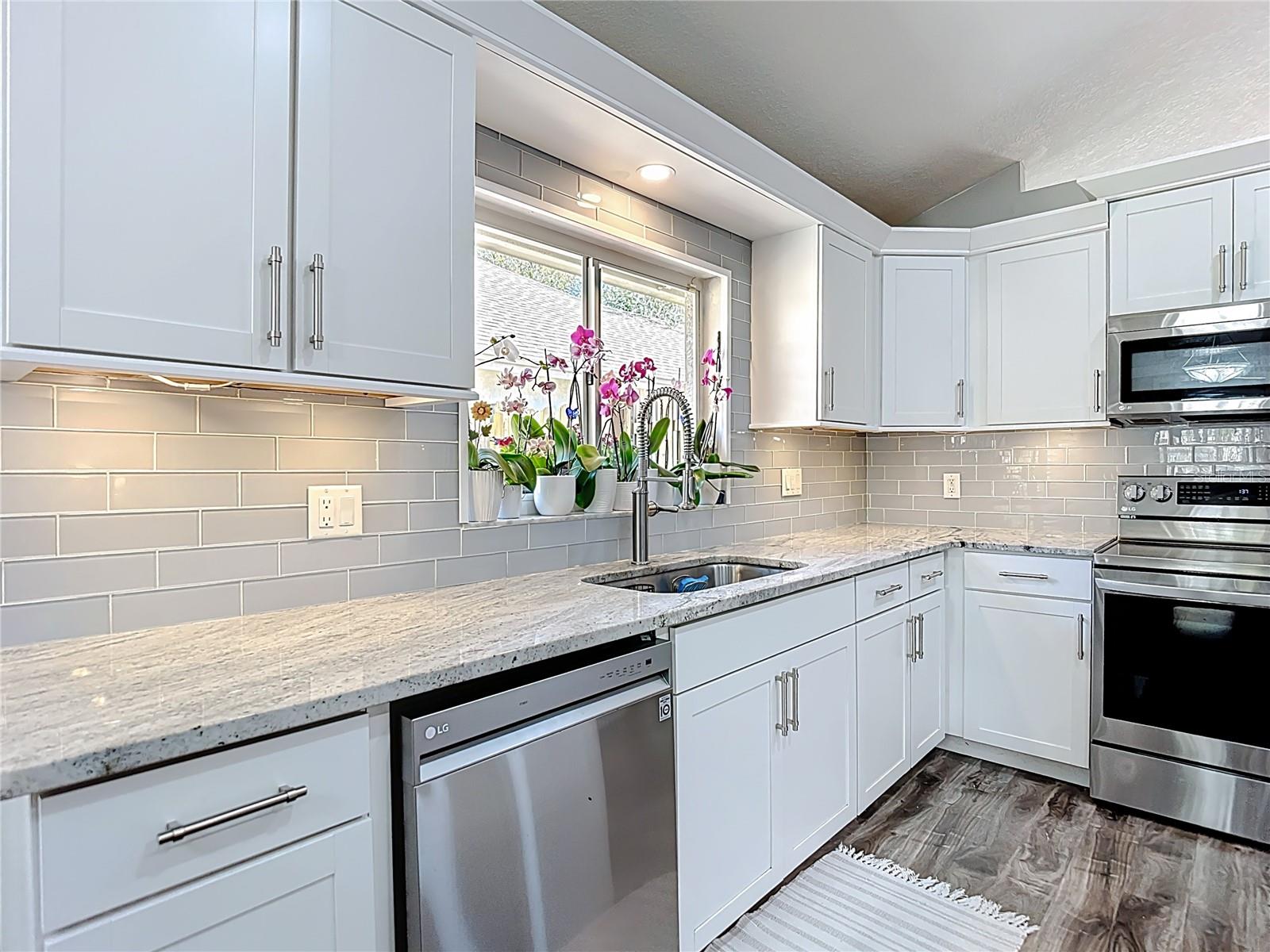 The fully remodeled kitchen (2021) is the heart of the home, featuring white cabinetry with modern hardware, granite countertops, glass subway tile backsplash, a large center island with built-in wine refrigerator, and stainless-steel LG appliances.