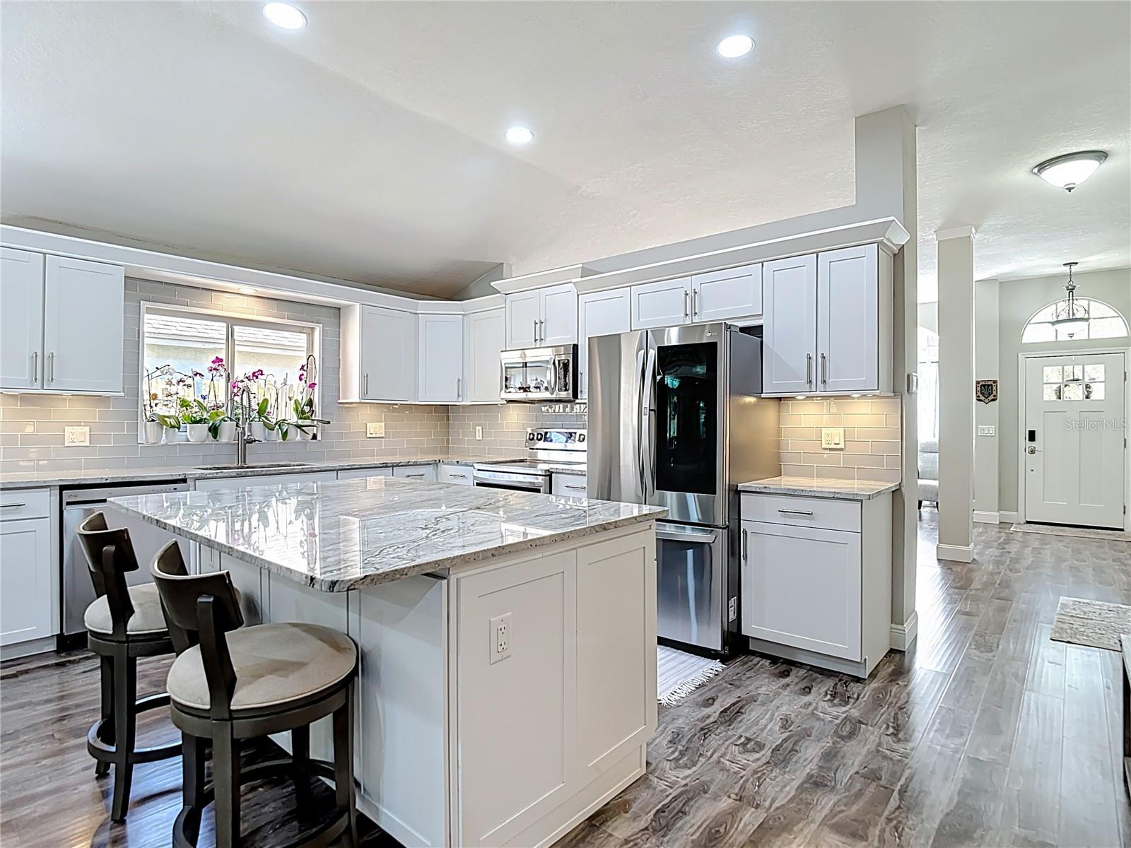 The fully remodeled kitchen (2021) is the heart of the home, featuring white cabinetry with modern hardware, granite countertops, glass subway tile backsplash, a large center island with built-in wine refrigerator, and stainless-steel LG appliances.