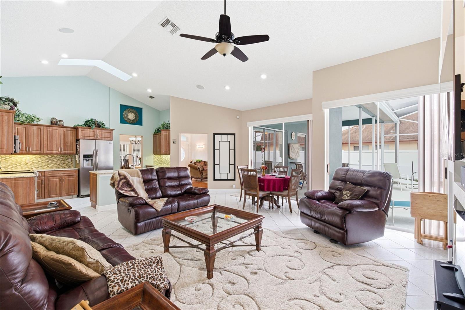 Open-concept great room with skylight and sliding doors overlooking the pool area.