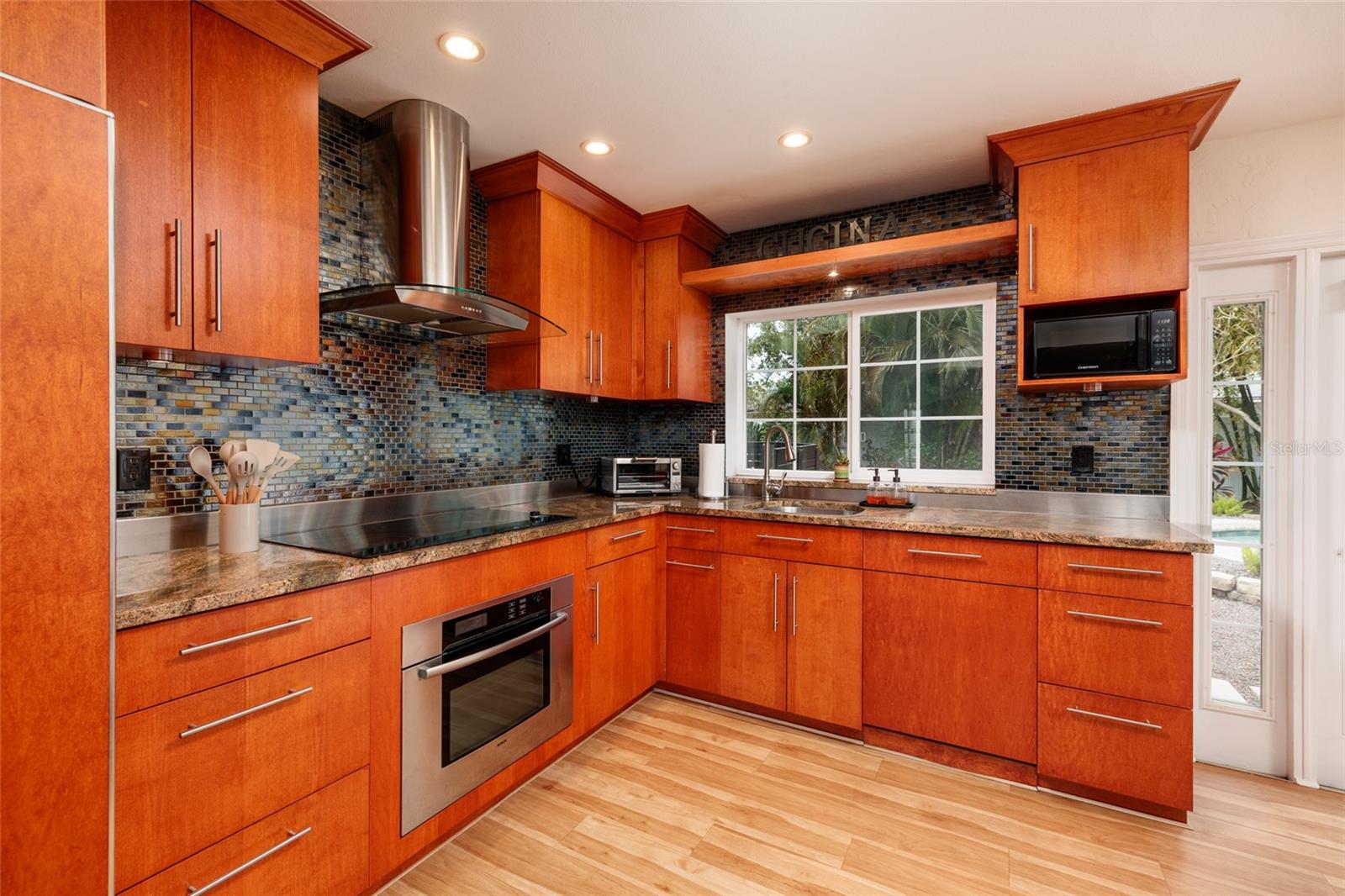 Clean, modern kitchen design with glass mosaic backsplash, designer range hood and under-cabinet lighting.