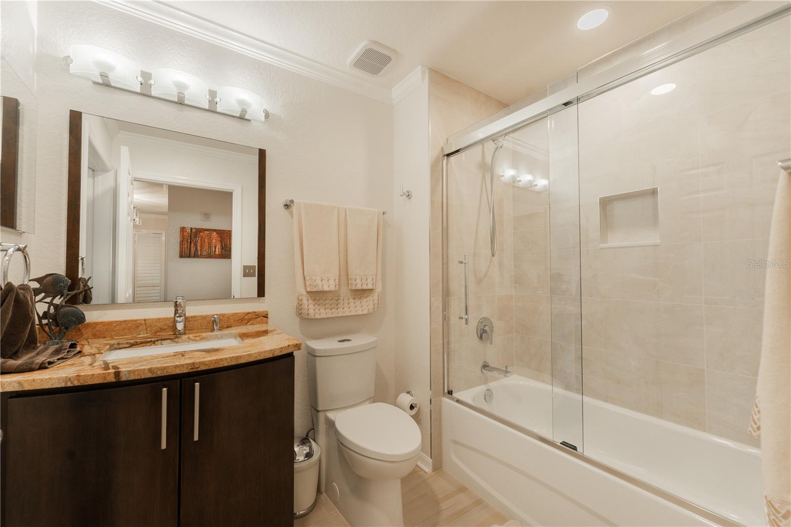 The second bathroom vanity and granite tastefully complement the kitchen, featuring a beautifully tiled shower, tub, and elegant glass shower doors.