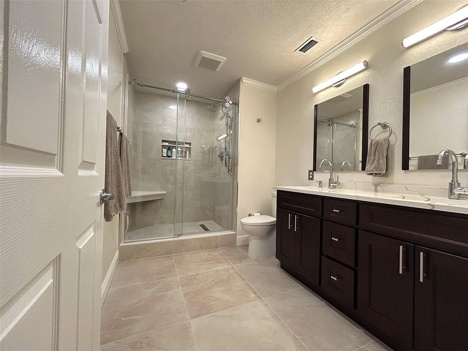 The luxurious primary en-suite bath boasts a spacious walk-in shower with elegant glass doors, a custom-built bench and niche, and an invigorating rain shower head.