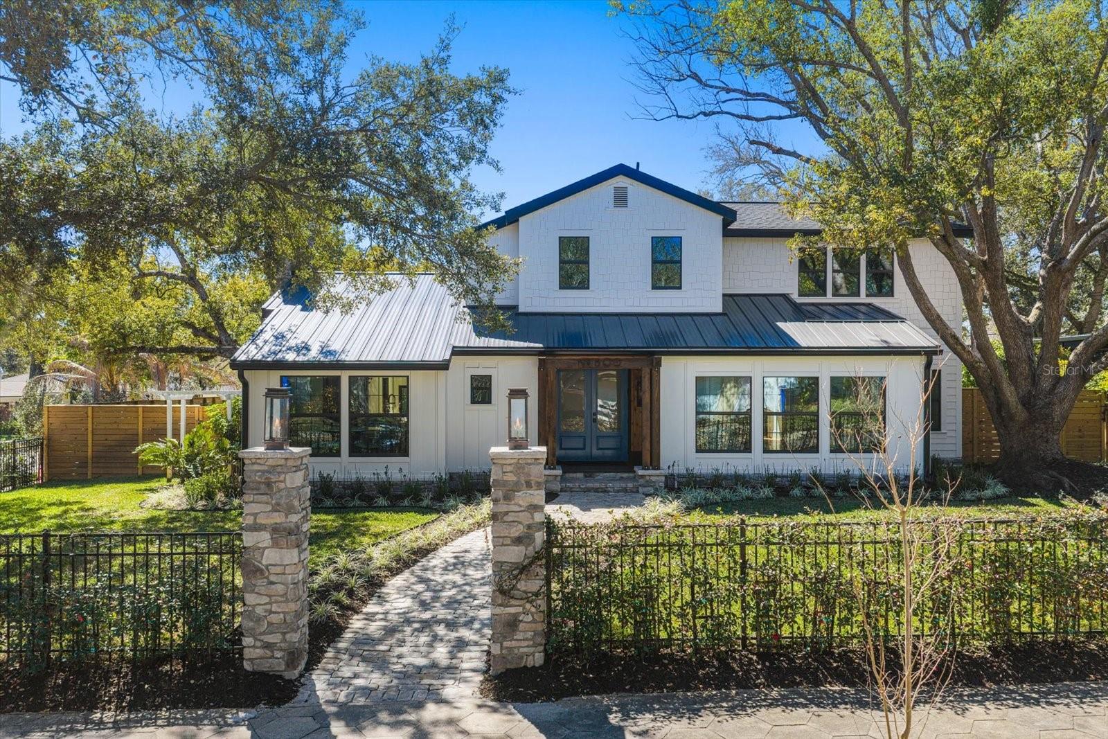 Front of home with stone walkway, gaslit stone pillars, wrought iron fencing with climbing jasmine, lushly landscaped yard