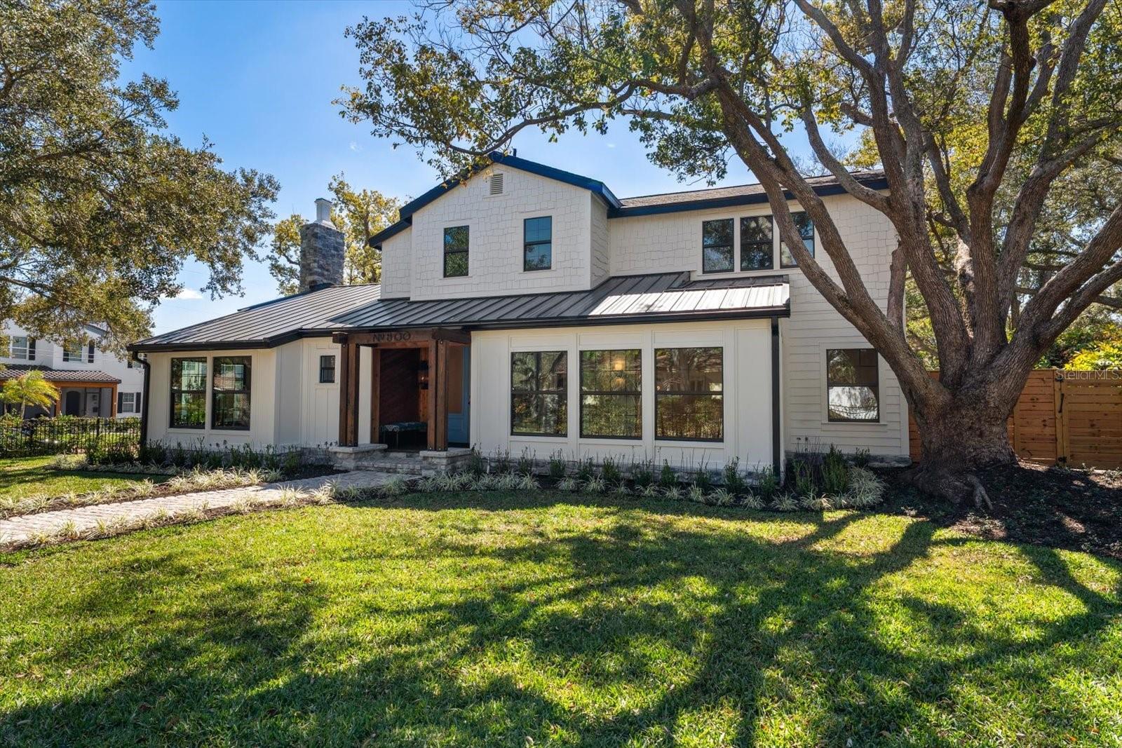Front of home with stone walkway,  lushly landscaped yard, shade trees