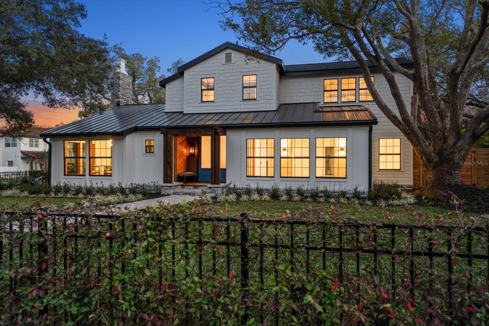 Front of home at twilight with stone walkway, wrought iron fencing with climbing jasmine, lushly landscaped yard, gas lanterns on front porch